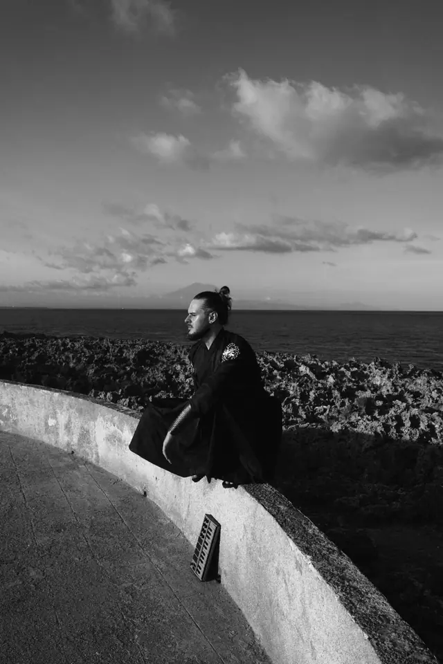 OPPAACHA sitting on a curved sea wall above the ocean, black and white