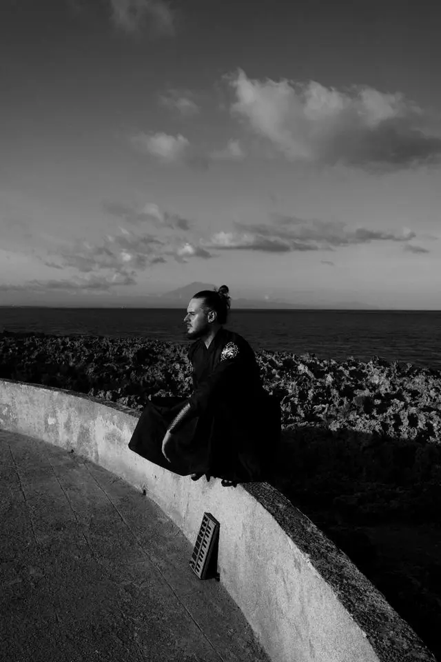 OPPAACHA sitting on a curved sea wall above the ocean, black and white
