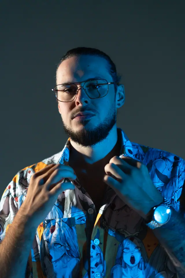Studio portrait of OPPAACHA in glasses and a patterned blue shirt